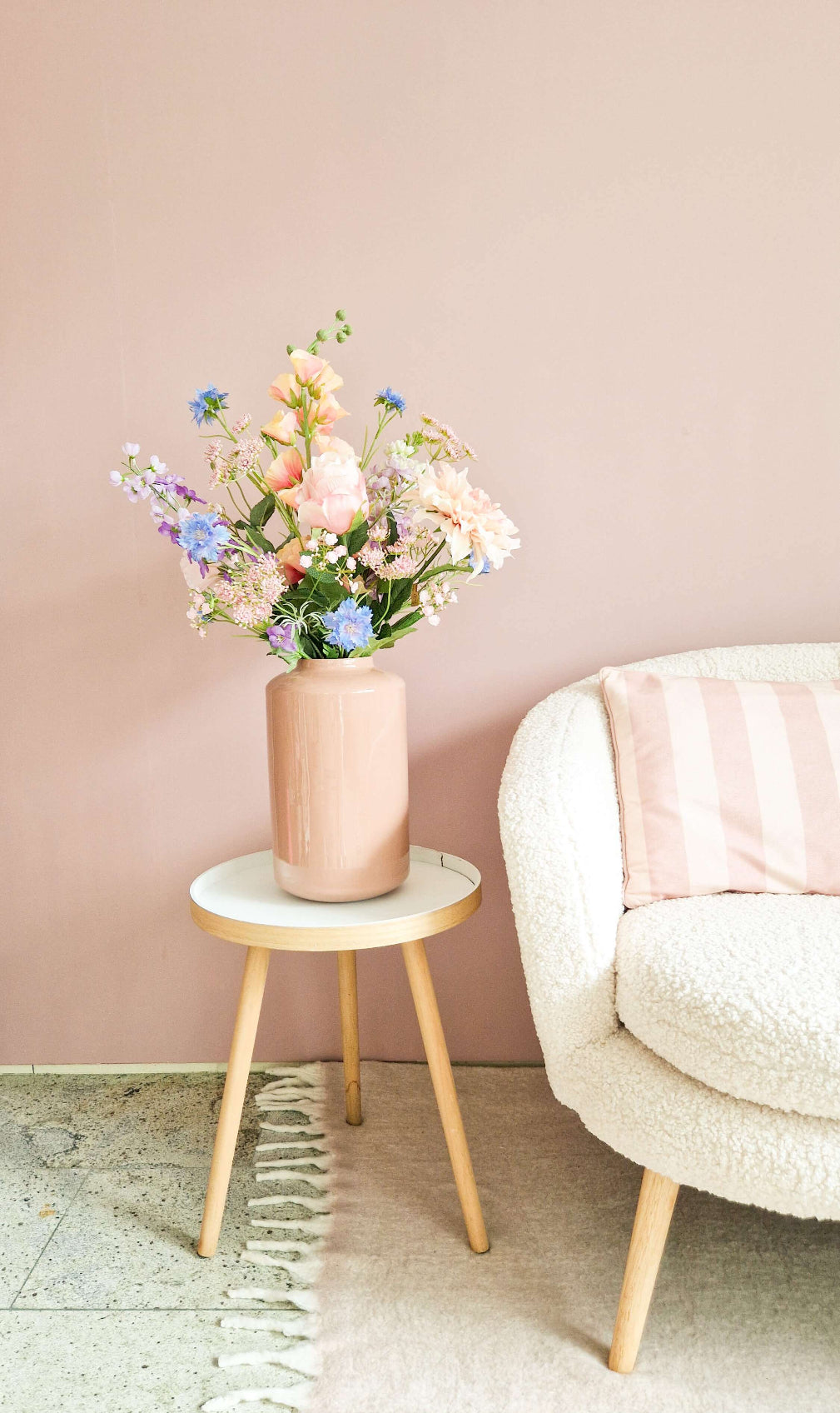 Zijden bloemenboeket in pastelkleuren in roze vaas op bijzettafel naast fauteuil