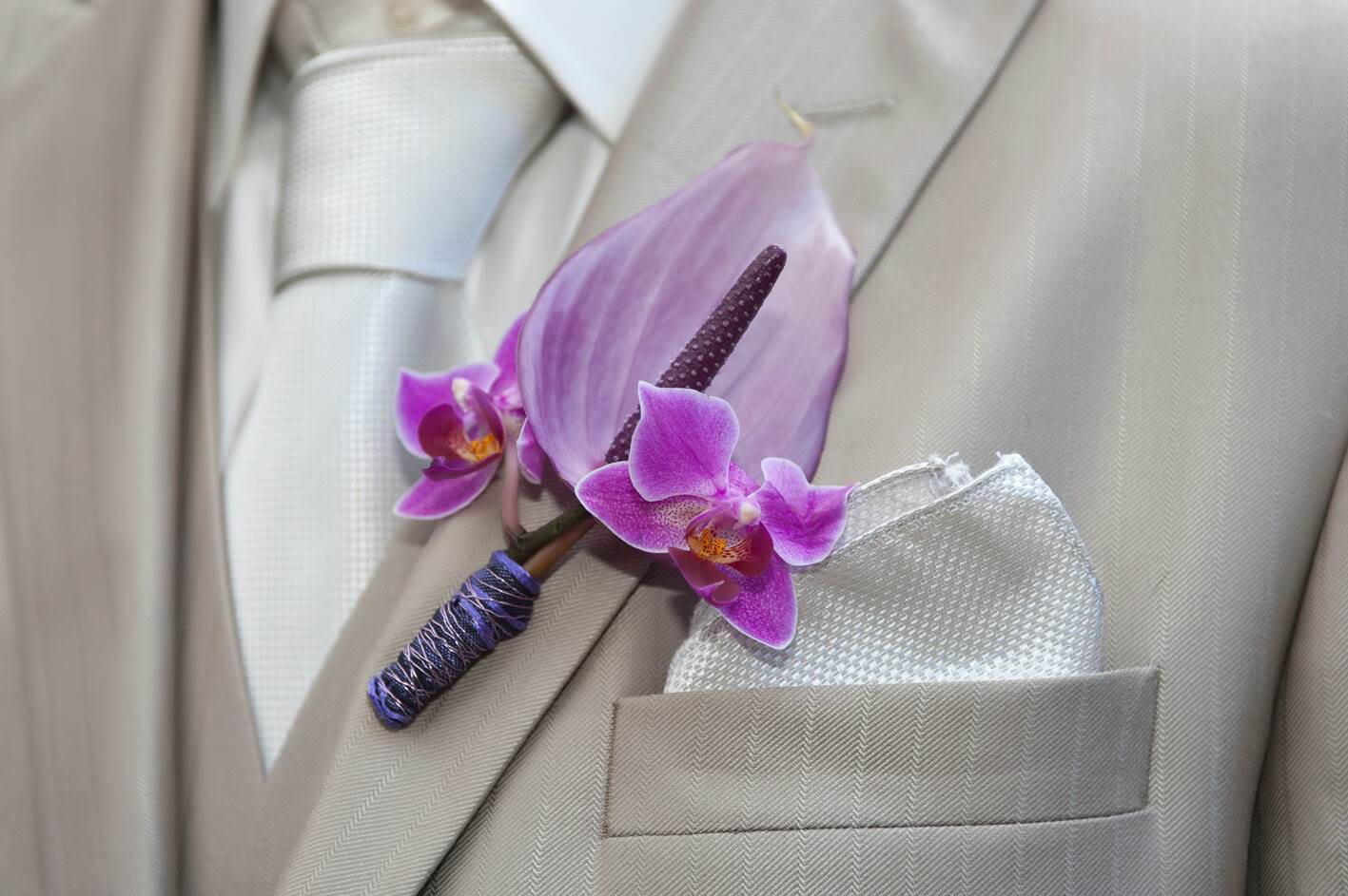 corsage voor bruidegom met roze bloemen als anthurium en orchidee afgewerkt met lint
