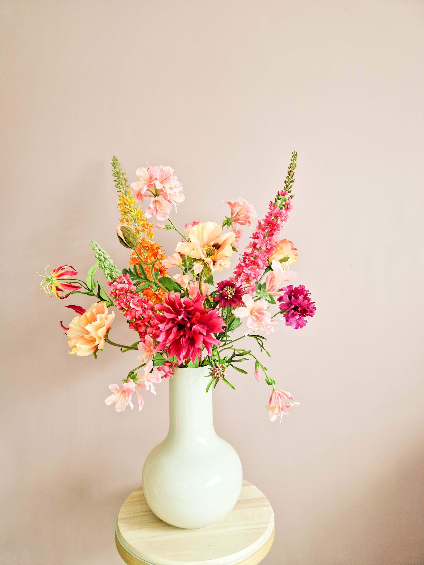 Zijden boeket met roze Dahlia’s, zalmkleurige Papaver, Rhododendron takken en oranje Eremurus in een vaas op een houten tafeltje.