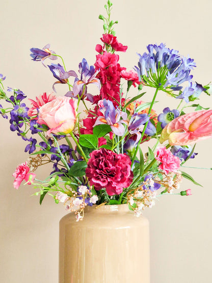 Zijden boeket met roze en paarse bloemen in roze vaas met o.a. anjer, roze delhinium, anthurium en iris. 
