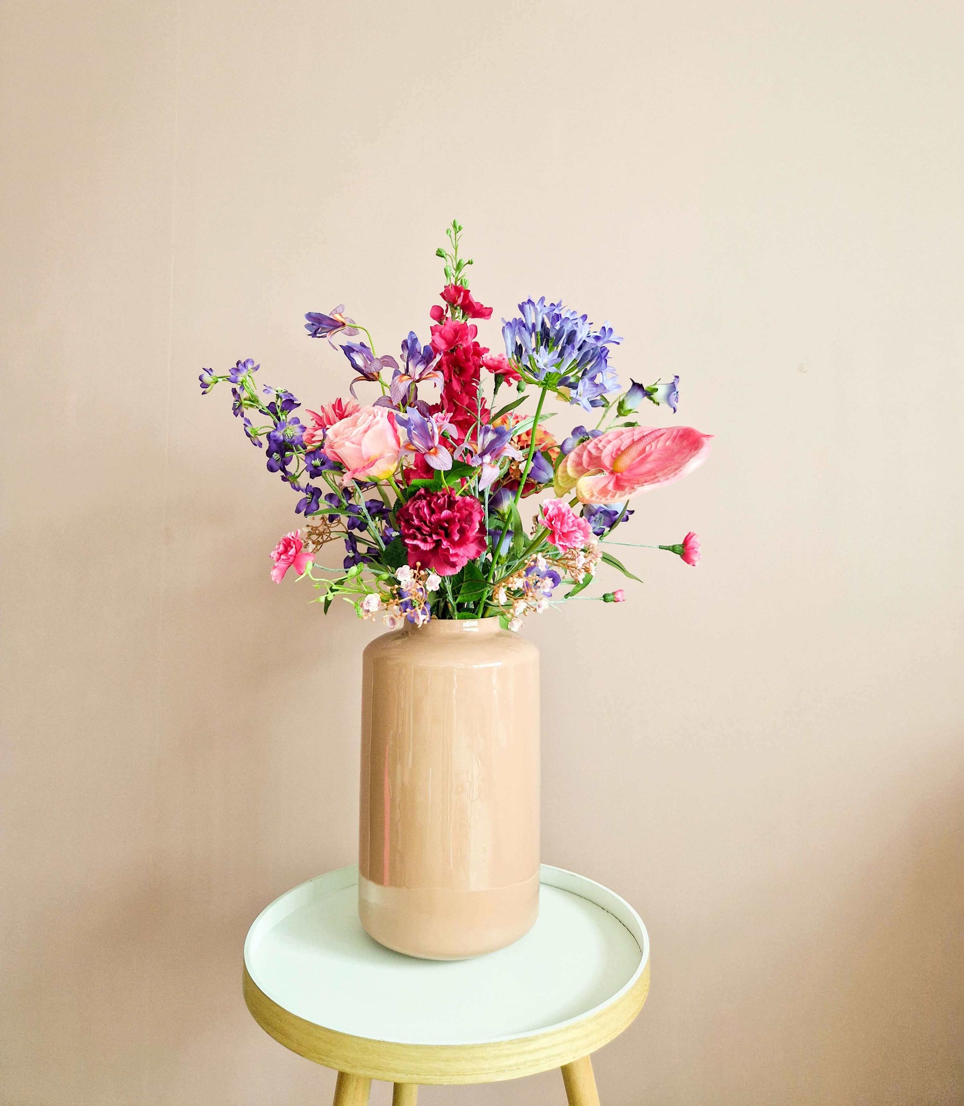 Zijden boeket met roze en paarse bloemen in roze vaas op houten tafeltje